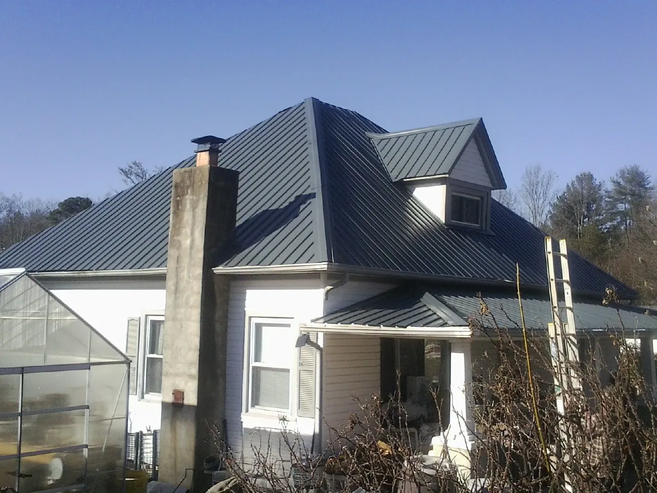 Dark blue standing seam metal roof on a white farmhouse with dormer — Slate & Tile Roof Repair by Roofing Brothers in Kensett