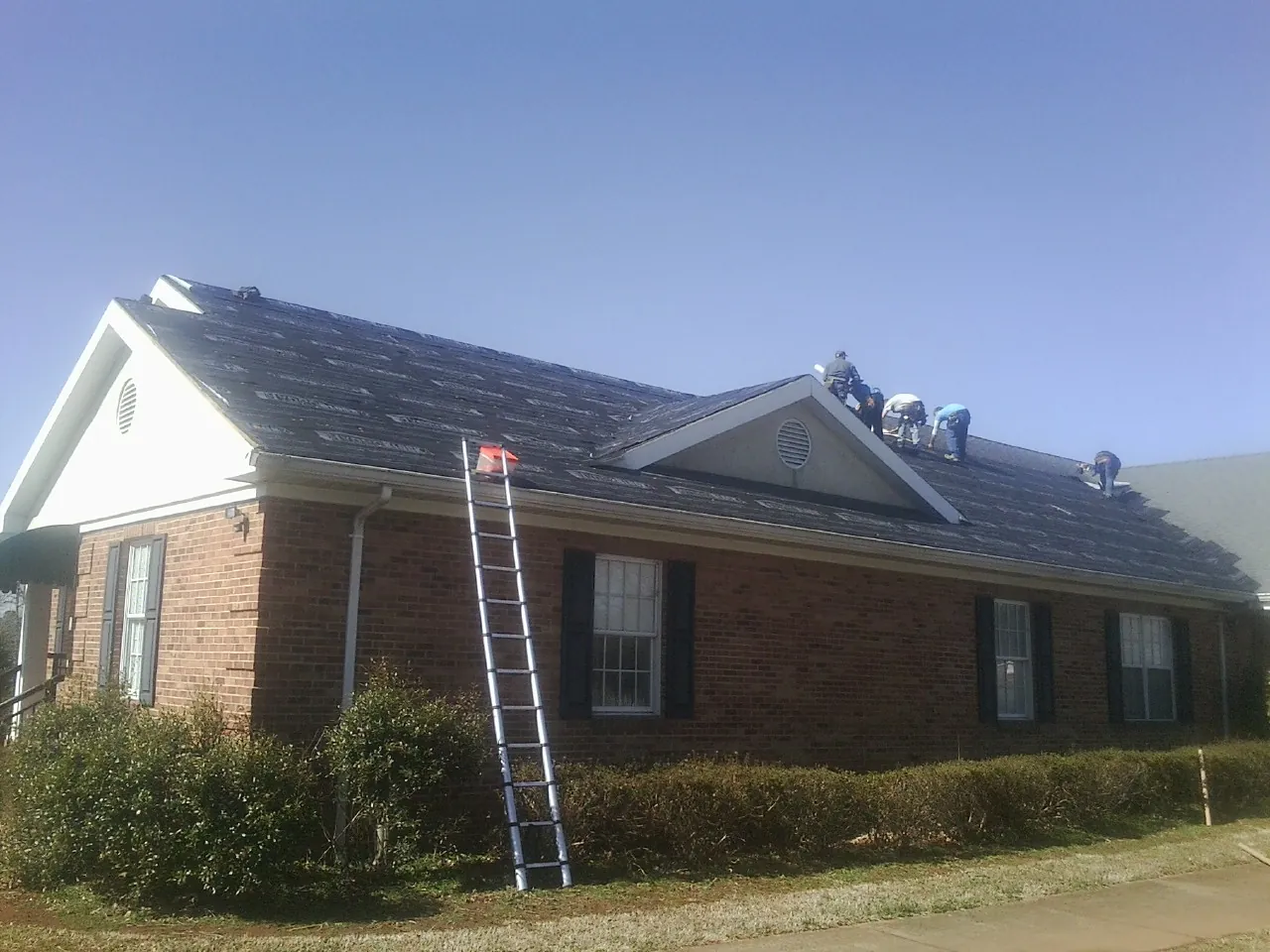 Crew tearing shingles off a brick ranch roof with a ladder set — Metal Roof Repair work by our crew in Kensett
