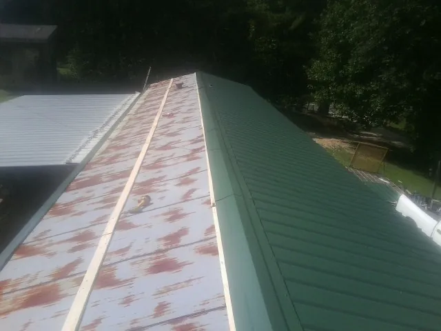 Old rusted panels beside newly installed green metal roofing — Wind Damage Roof Repair by Roofing Brothers in Kensett
