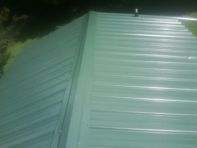 New green metal panels meeting at the ridge of a roof — Flat Roof Repair work by our crew in Kensett