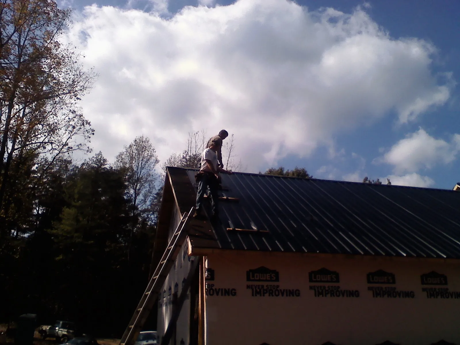Roofer fastening dark metal panels high against a cloudy sky, from a Roof Inspection job in Kensett