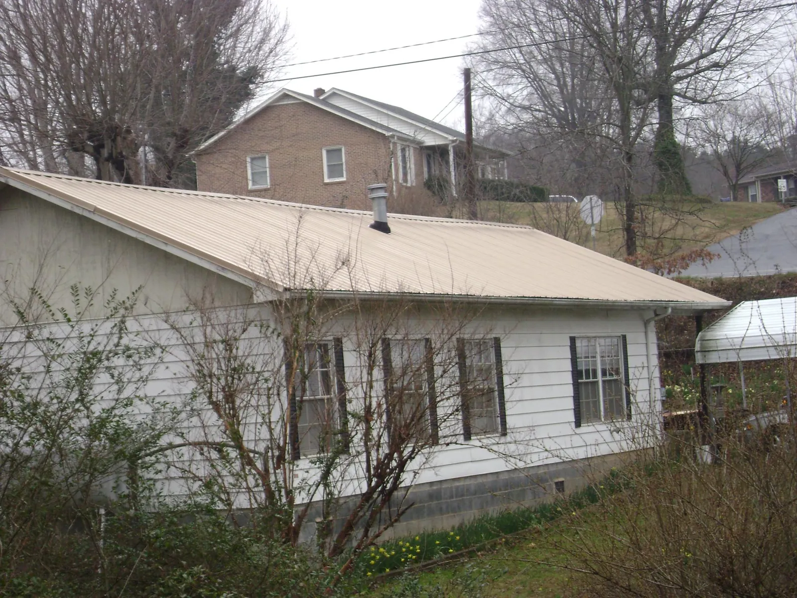 Tan metal roof on a white sided house set into a hillside — Commercial Roofing by Roofing Brothers in Kensett