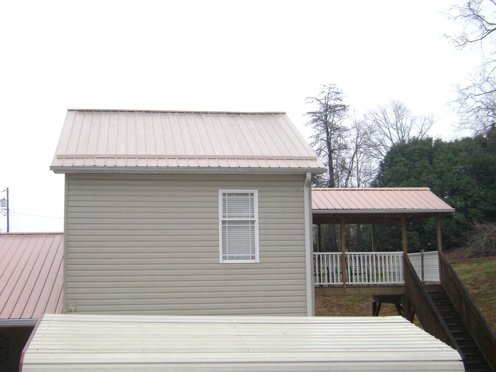 Tan metal roofs on a two story addition and attached porch, from a Roof Replacement job in Kensett